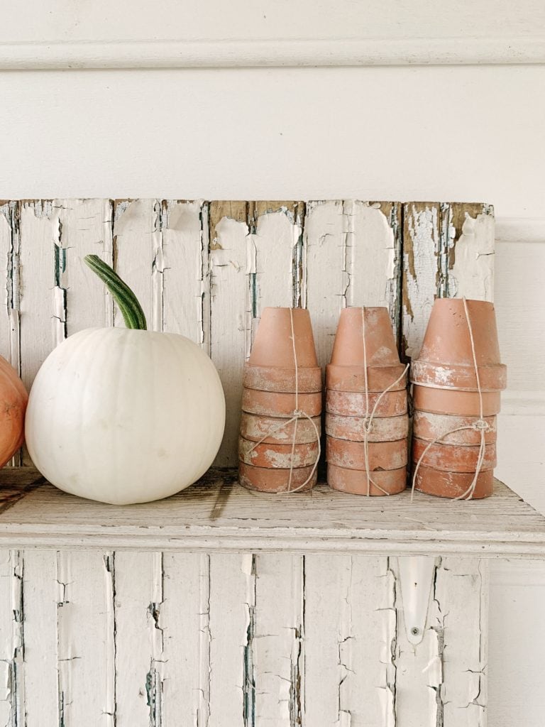 white pumpkin with terra cotta pots on chippy potting bench