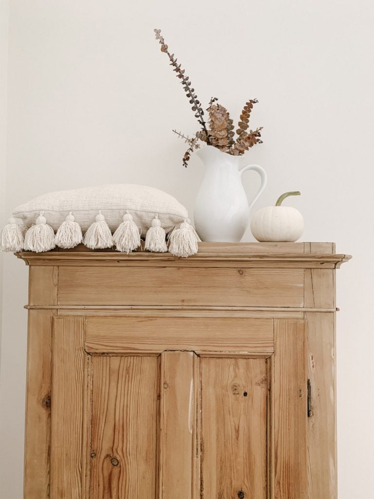 vase of orange eucalyptus with white pumpkin on top of an antique cabinet